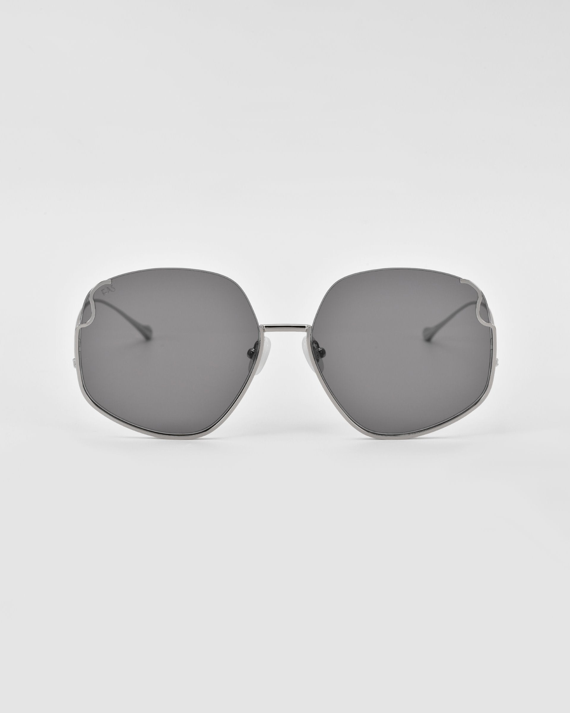A pair of luxurious Drape sunglasses from For Art's Sake® with large, dark tinted lenses and thin metal frames featuring intricate metal detailing. The design is minimalistic with clean lines, providing a sophisticated look. The background is plain white, highlighting the Drape sunglasses from For Art's Sake®.