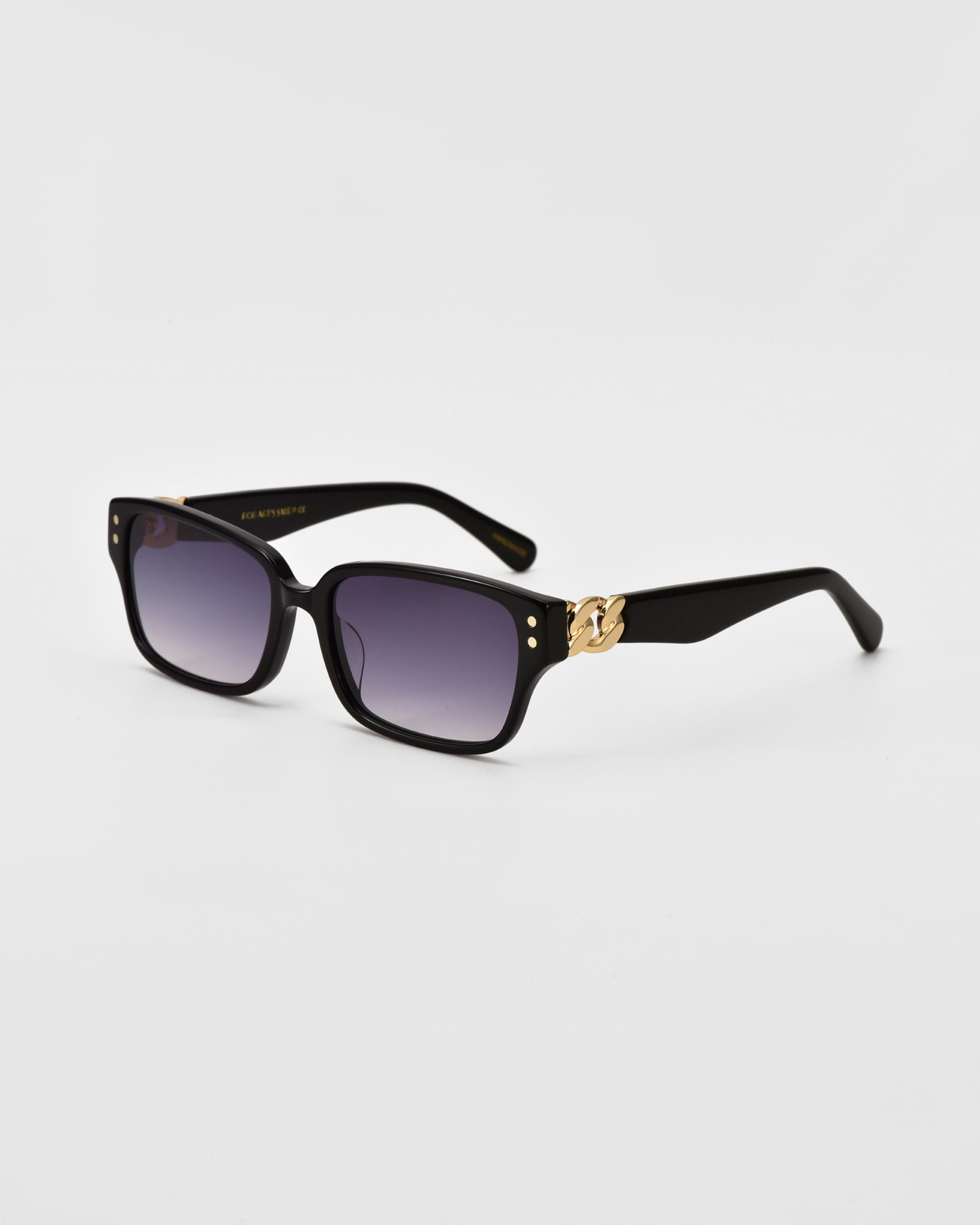 A pair of black rectangular For Art&#39;s Sake® Zenith sunglasses with dark tinted lenses is displayed against a plain white background. The handcrafted acetate sunglasses feature gold detailing on the temples near the hinges.