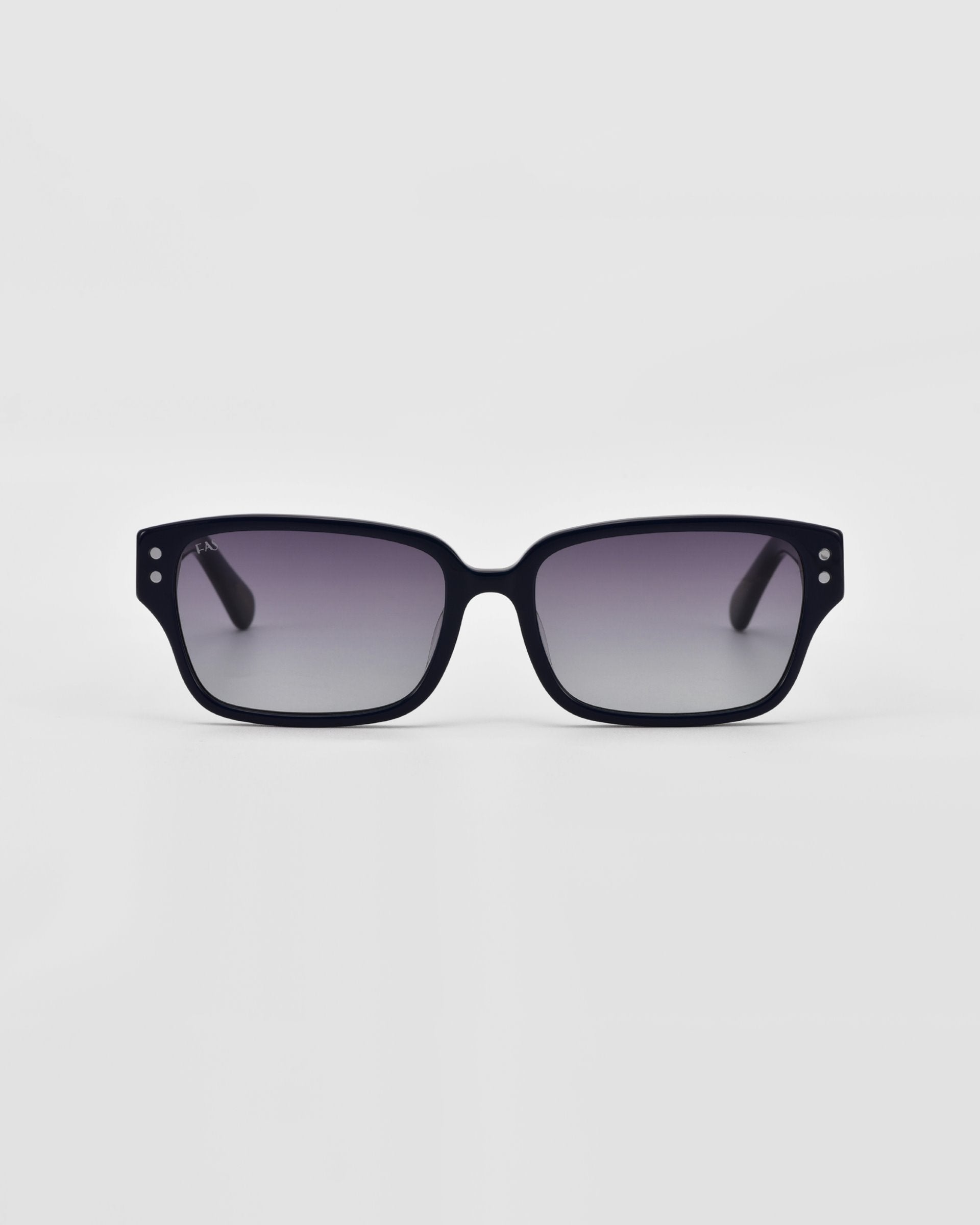 A pair of For Art&#39;s Sake® Zenith sunglasses with black rectangular frames made from handcrafted acetate stand against a plain, light grey background. Enhanced with sleek, slightly curved lines and chunky chain detailing, they exude a modern, stylish look.
