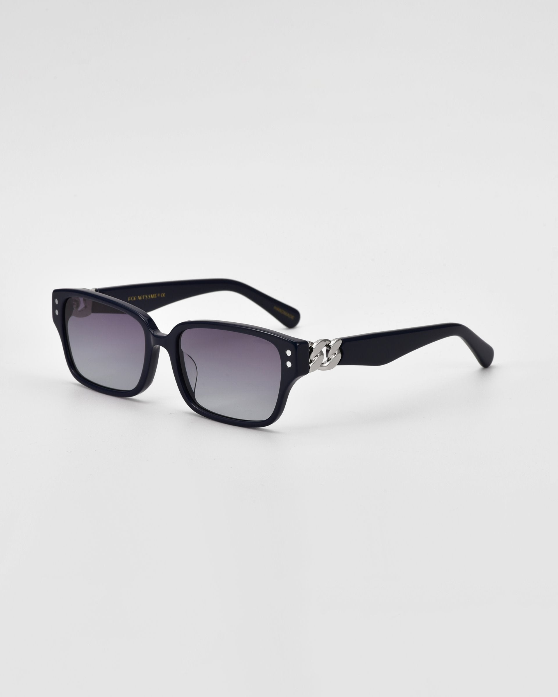The For Art&#39;s Sake® Zenith sunglasses are a pair of black rectangular shades with dark-tinted lenses. Handcrafted from acetate, the frame features small decorative details near the hinges and chunky chain detailing on the arms. These stylish sunglasses are set against a plain white background.