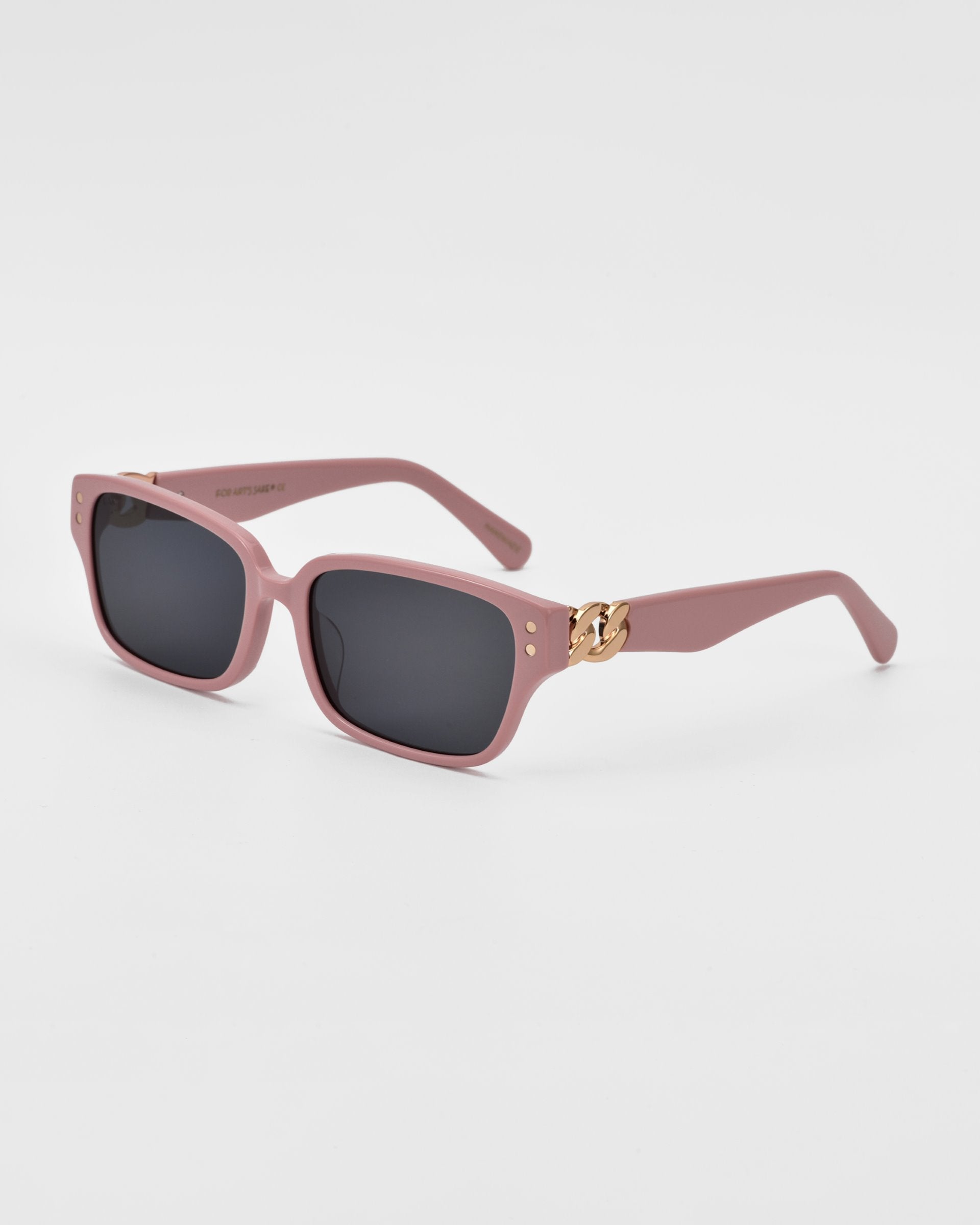 The For Art's Sake® Zenith sunglasses are a pair of pink rectangular sunglasses with dark lenses. Handcrafted from acetate, the frames feature a small, chunky chain detailing in gold on both sides near the temples, adding a decorative element against the white background.