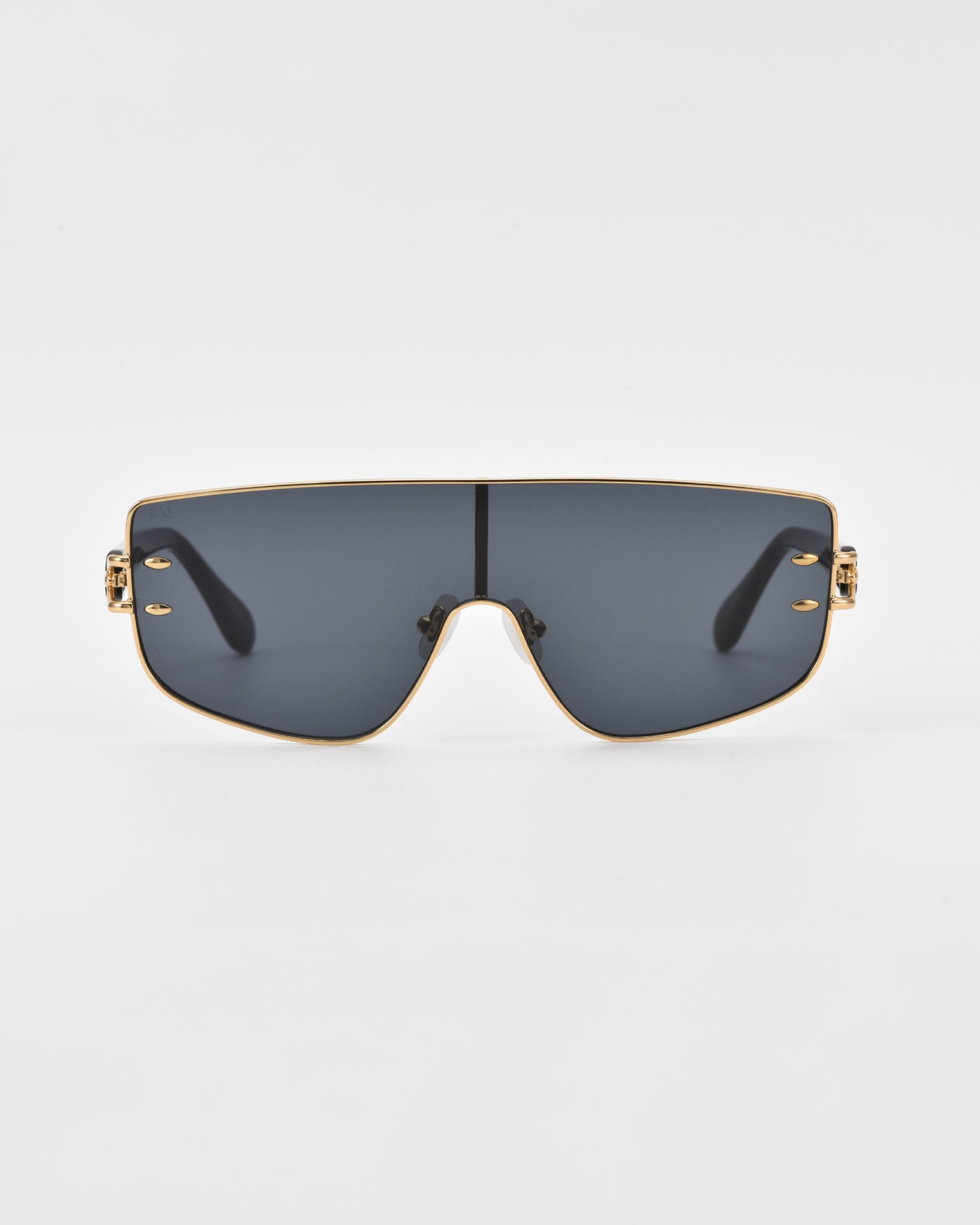 These For Art&#39;s Sake® Flare sunglasses feature oversized, dark-tinted lenses and a thin, gold-colored frame. With a flat-top design and decorative accents on the corners, they exude a futuristic design. The background is plain white.
