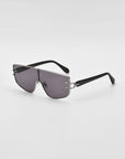 A pair of modern, angular For Art's Sake® Flare sunglasses with a silver metal frame, dark tinted rectangular lenses, and black arms. The futuristic design features a single, seamless lens spanning both eyes. Luxury eyewear set against a plain white background.