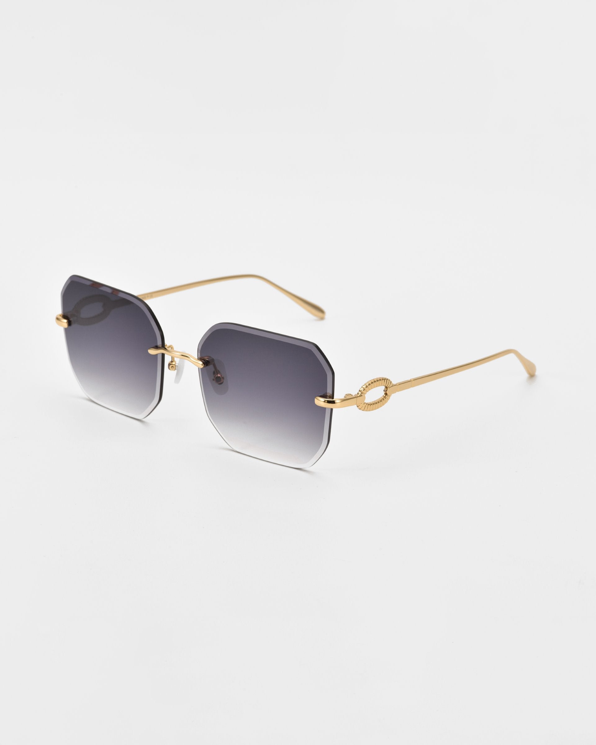 The Aria sunglasses by For Art&#39;s Sake® showcase stylish square, diamond-cut lenses with a gradient gray tint and thin gold arms. The arms feature a decorative loop detail near the hinges. Enhanced with jade-stone nose pads, these glasses are set against a plain white background.