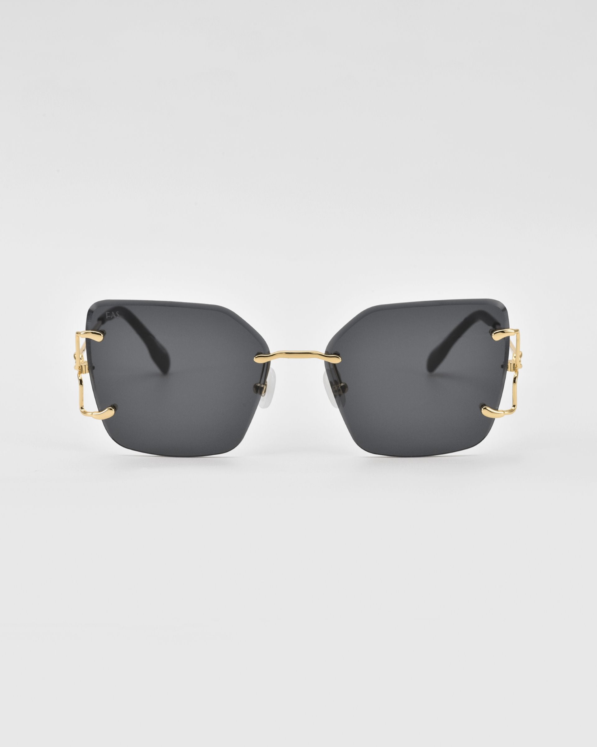 A pair of modern, oversized square lenses sunglasses with dark tinted lenses and gold-colored metal accents on the temples. The For Art's Sake® Starlit sunglasses feature jade-stone nosepads, and the minimalistic frame lacks a visible border around the lenses, creating a sleek and stylish design against a plain white background.