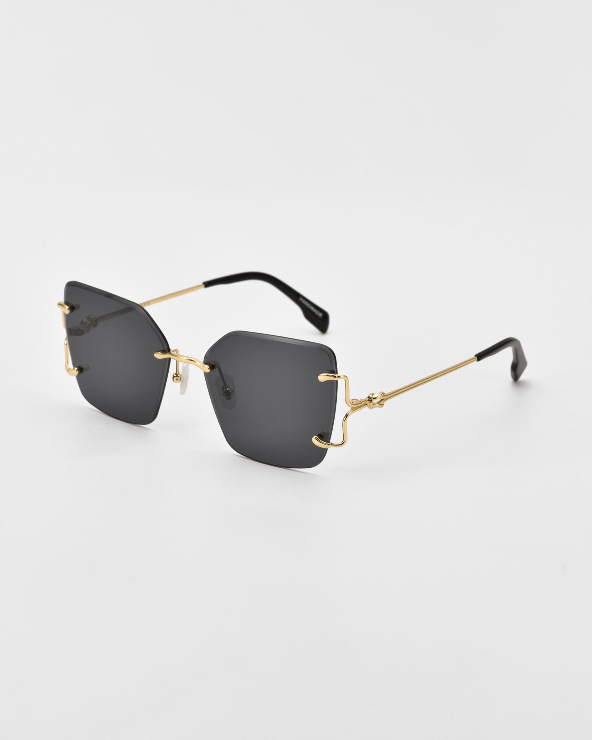 A pair of stylish For Art&#39;s Sake® Starlit sunglasses with dark, oversized square lenses and gold-tone, wireframe temples. The design is minimalistic with a modern aesthetic, featuring black temple tips and jade-stone nosepads. The background is plain white.