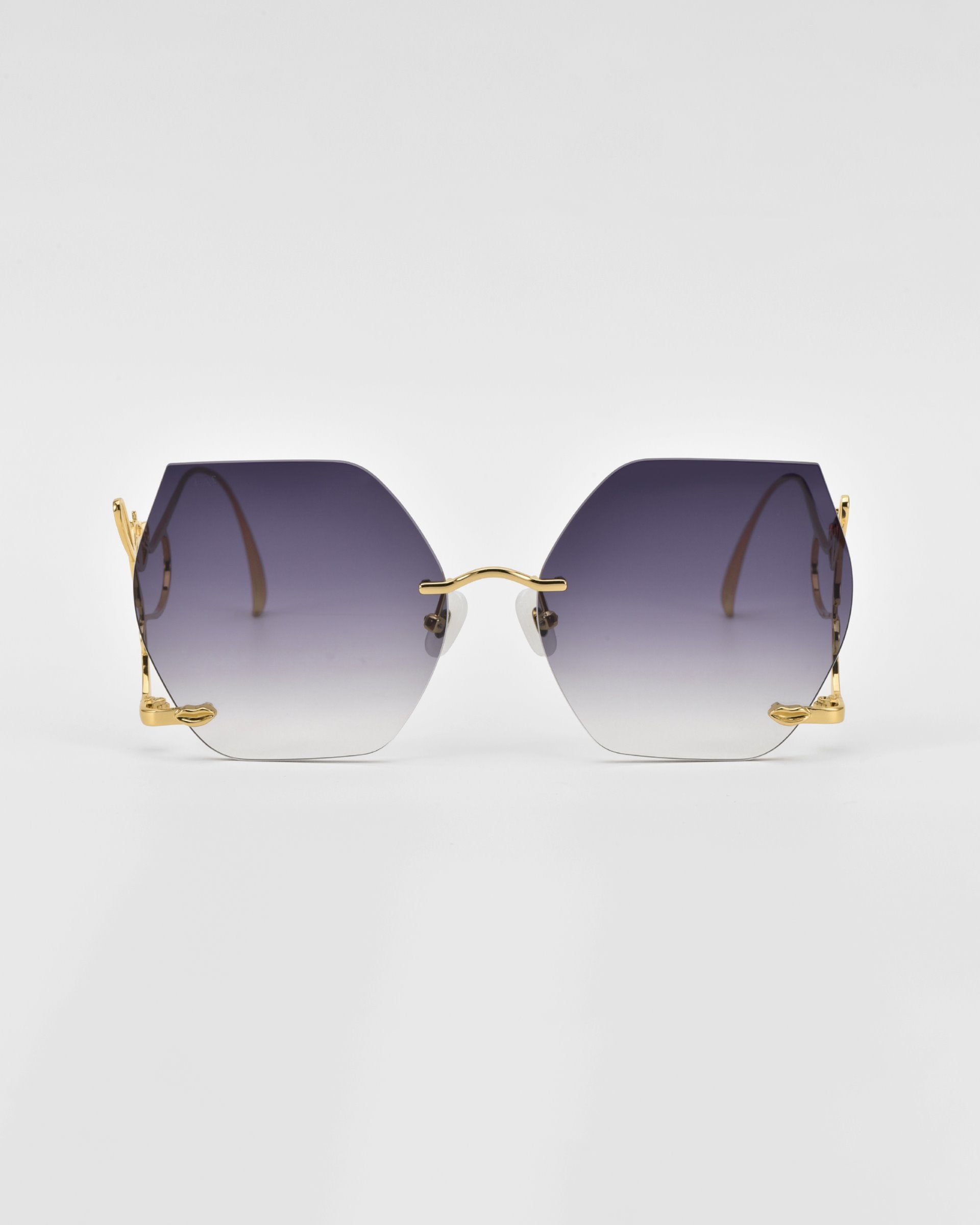 A pair of Cry Me a River sunglasses from For Art&#39;s Sake® with gradient hexagonal lenses, transitioning from dark purple to lighter shades at the bottom, featuring thin gold frames and temples, lying flat against a plain white background. These limited edition sunglasses are truly one-of-a-kind.