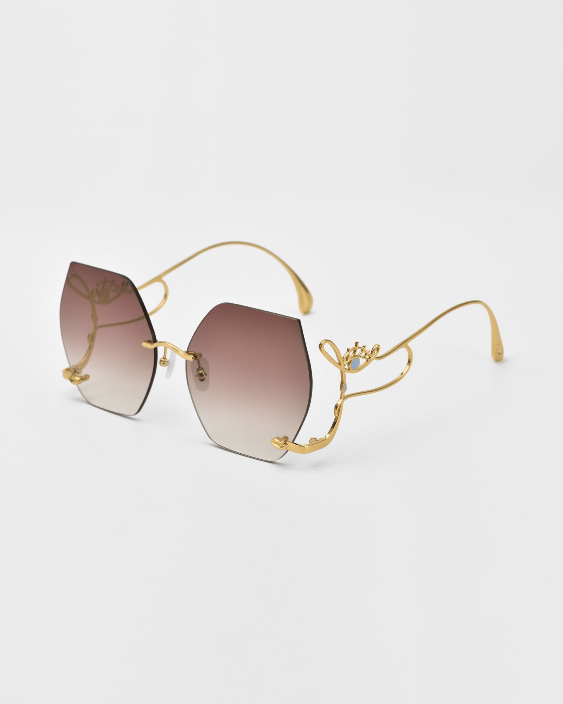 A pair of stylish, limited edition Cry Me a River sunglasses by For Art&#39;s Sake® with gradient brown lenses and intricate gold frames. The unique frame design features delicate, floral-like embellishments on the arms, providing a luxurious and elegant appearance against a plain white background.