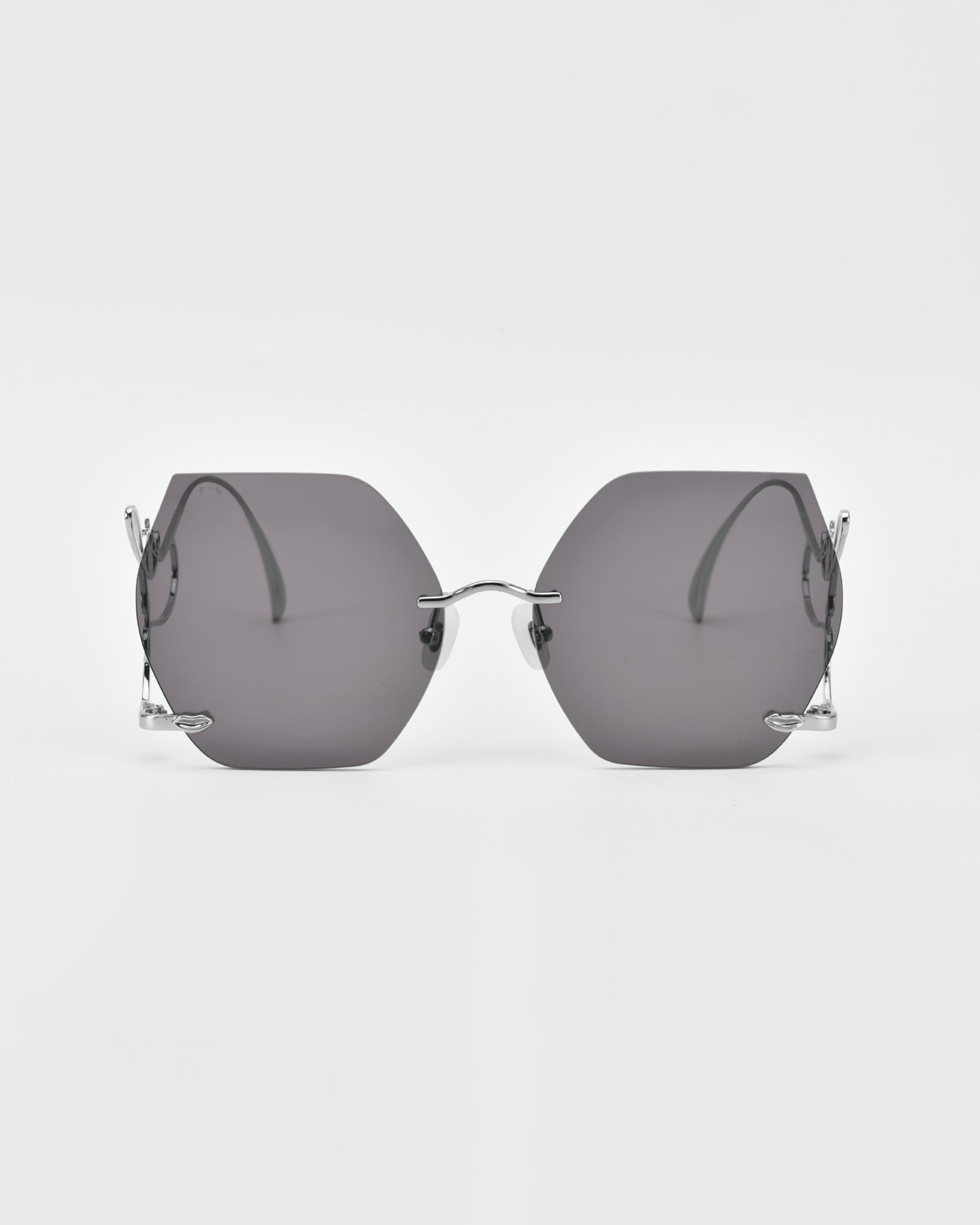 A pair of stylish, rimless, hexagon-shaped sunglasses with dark tinted lenses and thin metal arms. These limited edition Cry Me a River sunglasses by For Art&#39;s Sake® stand out against the white background, highlighting their sleek design and modern aesthetic.