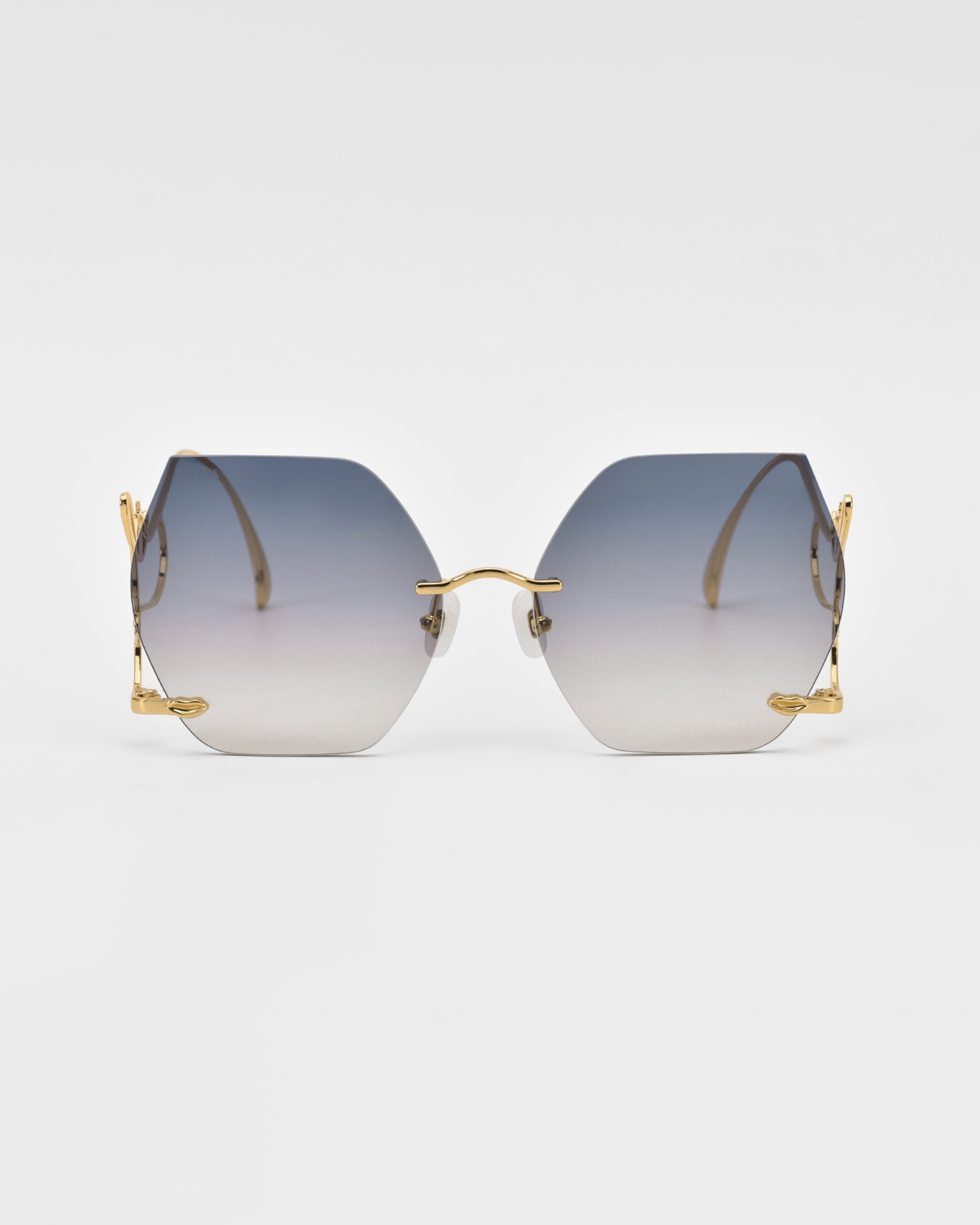 A pair of For Art&#39;s Sake® Cry Me a River hexagonal gradient sunglasses with gold frames is displayed against a plain white background. The lenses transition from dark at the top to nearly clear at the bottom, and the thin arms feature intricate detailing near the hinges.