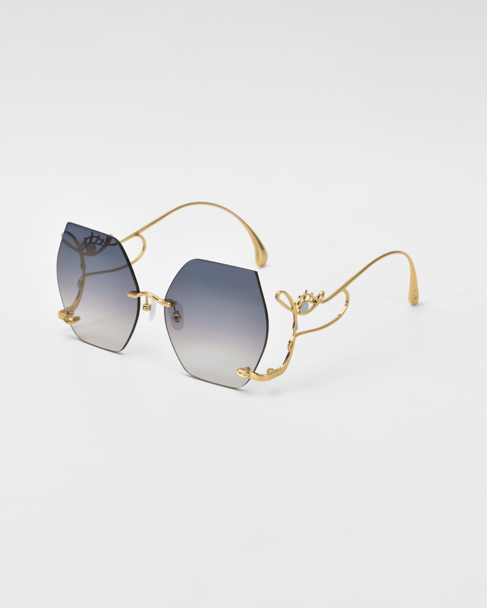 Introducing the For Art&#39;s Sake® Cry Me a River sunglasses: a pair of limited edition, stylish sunglasses featuring hexagonal gradient lenses transitioning from dark to light. The frame is gold with delicate, ornate detailing on the arms and bridge. The tips of the arms are elegantly curved, lending a sophisticated look.