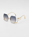 Introducing the For Art's Sake® Cry Me a River sunglasses: a pair of limited edition, stylish sunglasses featuring hexagonal gradient lenses transitioning from dark to light. The frame is gold with delicate, ornate detailing on the arms and bridge. The tips of the arms are elegantly curved, lending a sophisticated look.