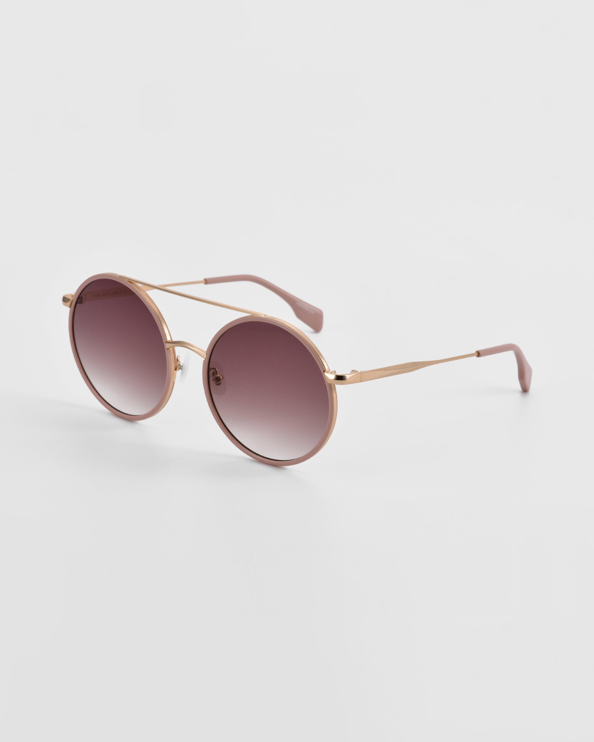 A pair of oversized round aviator sunglasses with a rose gold metal frame and gradient lenses transitioning from dark purple to light pink. Featuring jade-stone nose pads, the arms have brown tips, and the For Art&#39;s Sake® Orb sunglasses are positioned on a plain white background.