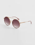 A pair of oversized round aviator sunglasses with a rose gold metal frame and gradient lenses transitioning from dark purple to light pink. Featuring jade-stone nose pads, the arms have brown tips, and the For Art's Sake® Orb sunglasses are positioned on a plain white background.