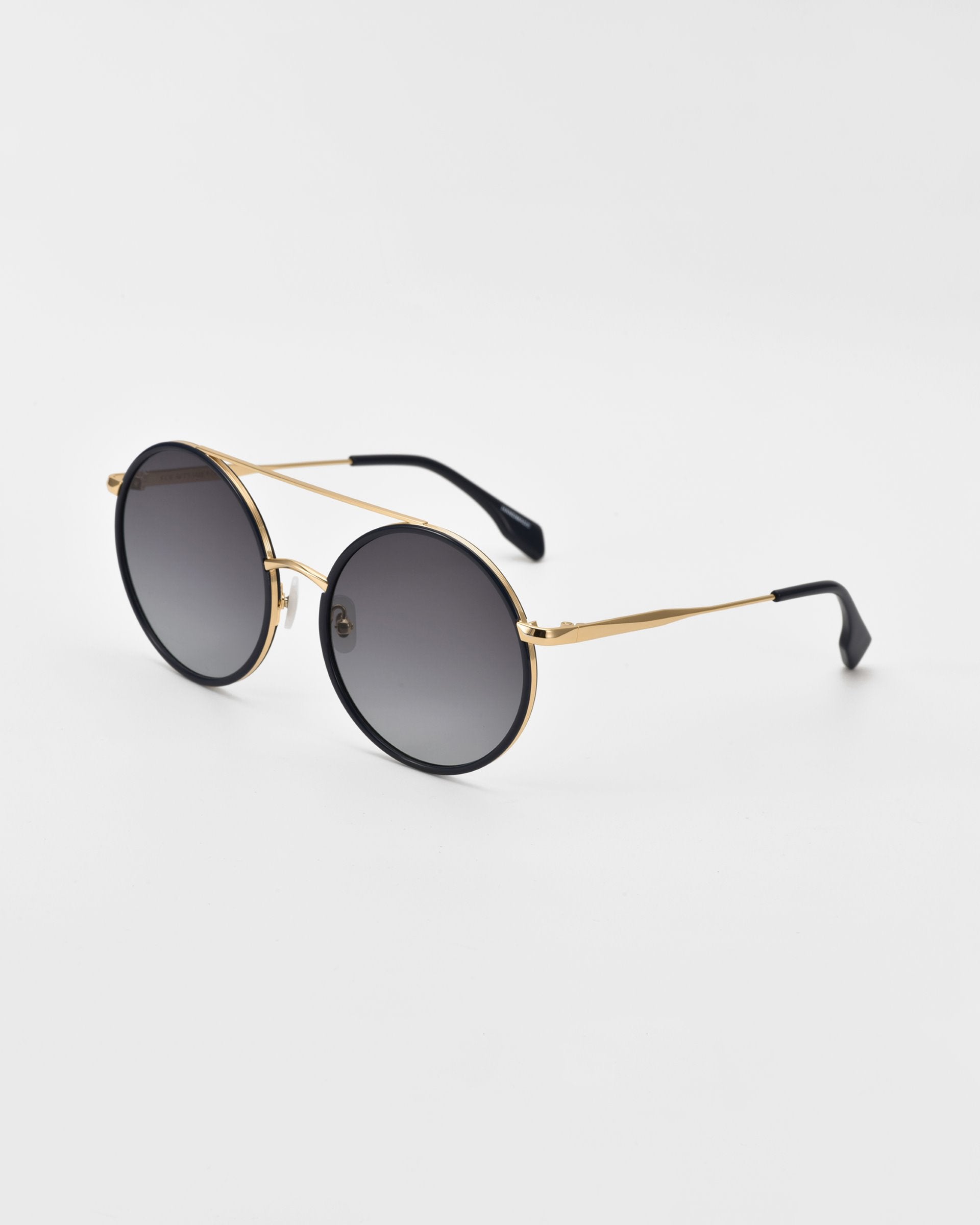 A pair of oversized round aviator sunglasses with black lenses and thin gold-colored frames. The temples feature black ear pieces, and the jade-stone nose pads enhance comfort. The plain white background accentuates the sleek design of these chic Orb sunglasses by For Art&#39;s Sake®.