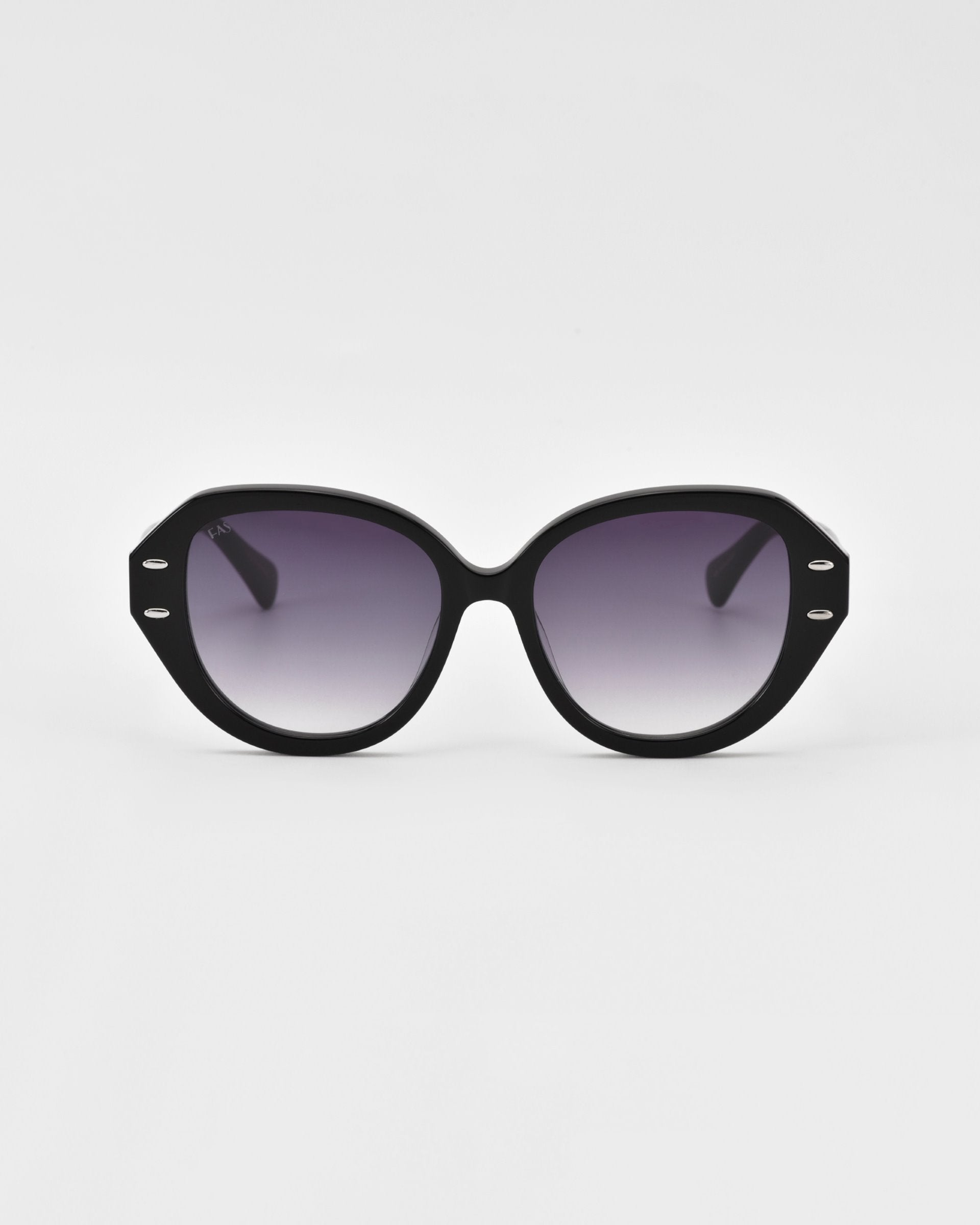 A pair of black oversized cat-eye Mirage sunglasses from For Art&#39;s Sake® with dark gradient lenses and silver accents on the temples. The frame, crafted from plant-based acetate, boasts a slightly geometric shape and is set against a plain white background.