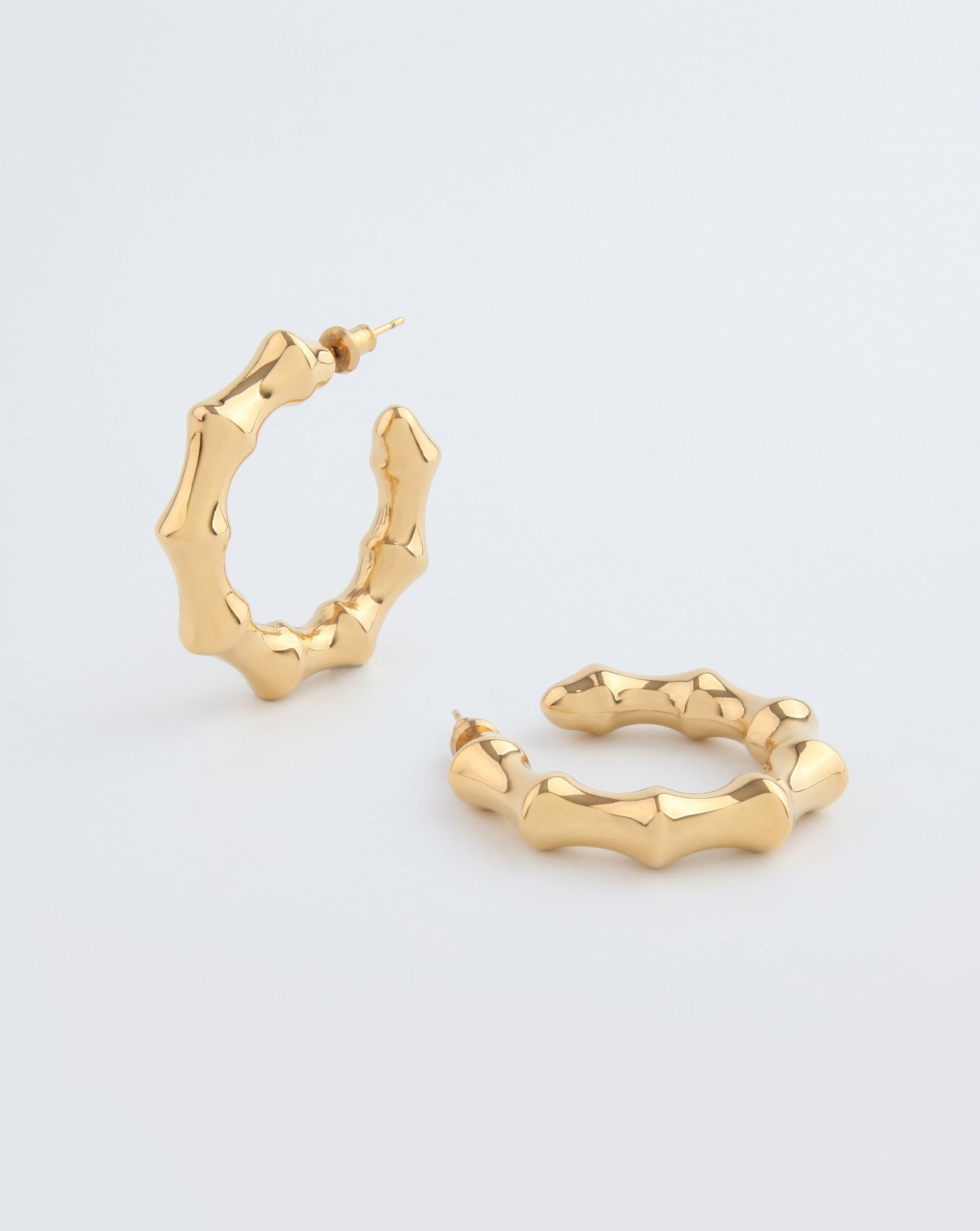 A pair of Bamboo Earrings Gold from For Art's Sake® with a unique, wavy, and textured design. Featuring a shiny finish and post-back fastening, they are displayed on a plain white background, with one standing upright and the other lying flat.