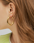 Close-up of a person's ear showcasing a large, smooth, For Art's Sake® Oval Earrings Silver. The individual has light brown hair and is wearing a light green top with a silver beaded neckline. The background is a plain, light gray color.