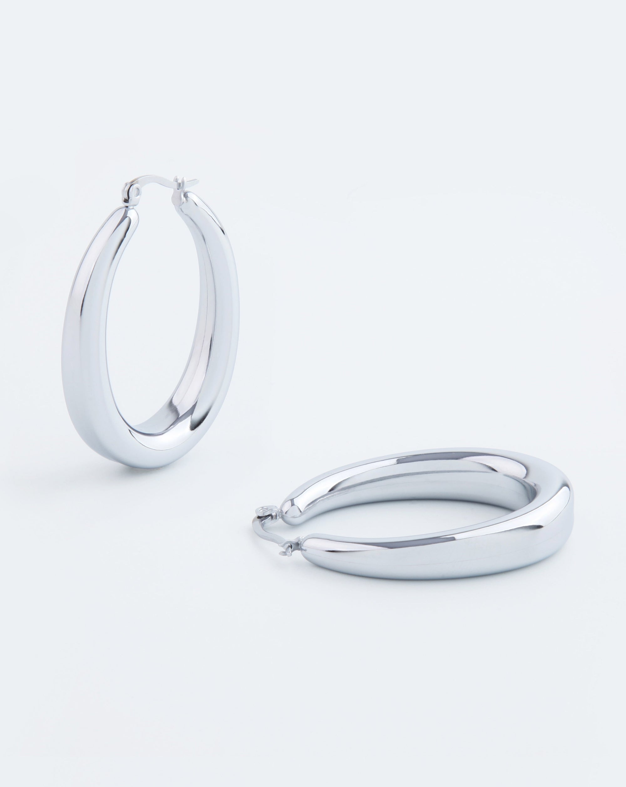 A pair of 18kt gold-plated Oval Earrings Silver by For Art's Sake® is shown against a plain white background. One earring stands upright, while the other lies flat, showcasing their glossy, polished finish. The simplistic design emphasizes their sleek, rounded shape.