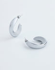 A pair of stylish, chunky Wave Earrings Silver by For Art's Sake® with a unique, open-ended design. The metallic surface has a polished, reflective finish. The earrings are positioned on a plain white background, one standing upright and the other lying flat.